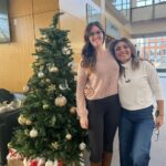 Two women standing next to a christmas tree.